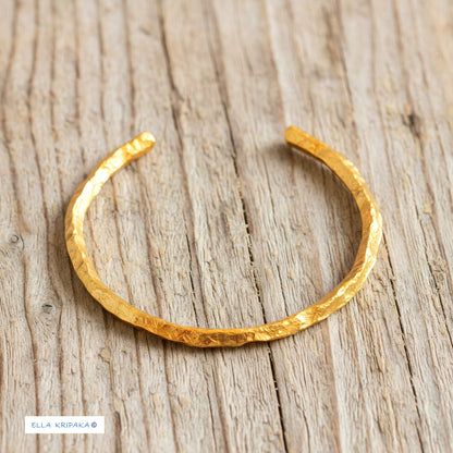Organic hammered 24k 9999 gold bracelet uneven cuff on a old wooden background, branding artist-jeweler name 'Ella Kripaka'