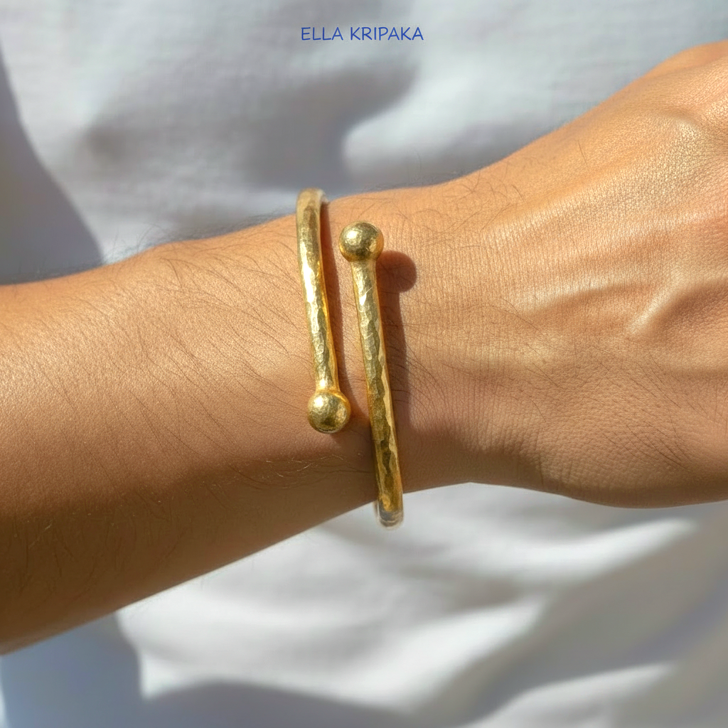 Twisted 24k gold hammered bracelet with convex round ends is worn by a man on wrist and on white blurred background, branded artist 'Ella Kripaka'