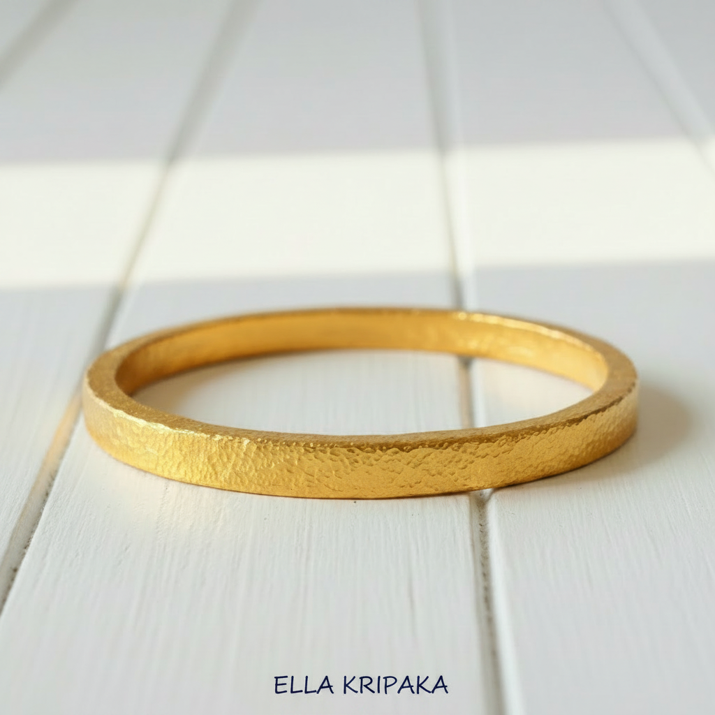 Hammered 24k 9999 gold bangle thick bracelet Ancient Rome style on a white wooden background, artist-jeweler name 'Ella Kripaka' branding