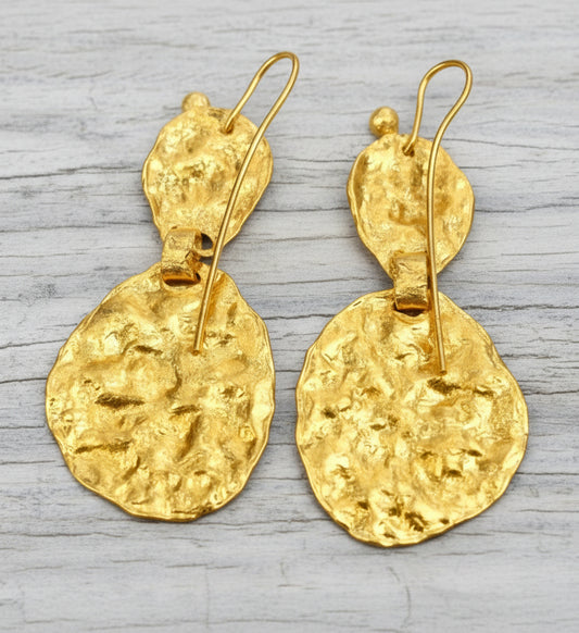 Organic 24k gold hammered uneven earrings wuth shiny wavy textures on backside are on light grey rustic wooden background, branding artist-jeweler 'Ella Kripaka'