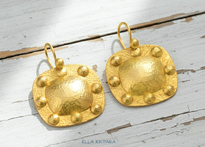 Solid 24k 9999 gold hammered Byzantine convex square earrings with hook clasps and shiny forged gold textures on old wooden background , artist's name 'ELLA KRIPAKA'