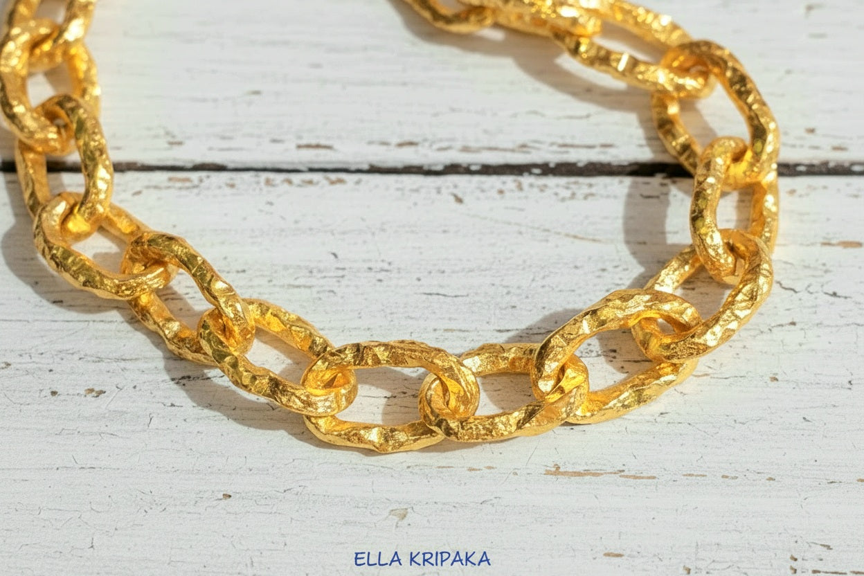 Hammered 24k 9999 gold organic chain with hammered uneven textures and a thick hook clasp on a white old wooden surface, artist name 'Ella Kripaka'