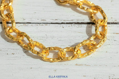 Hammered 24k 9999 gold organic chain with hammered uneven textures and a thick hook clasp on a white old wooden surface, artist name 'Ella Kripaka'