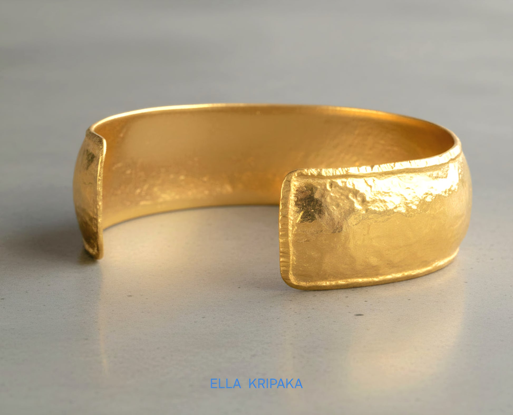 24k 9999 gold hammered Ancient Rome convex  cuff bracelet on a grey concrete surface, branded 'Ella Kripaka'