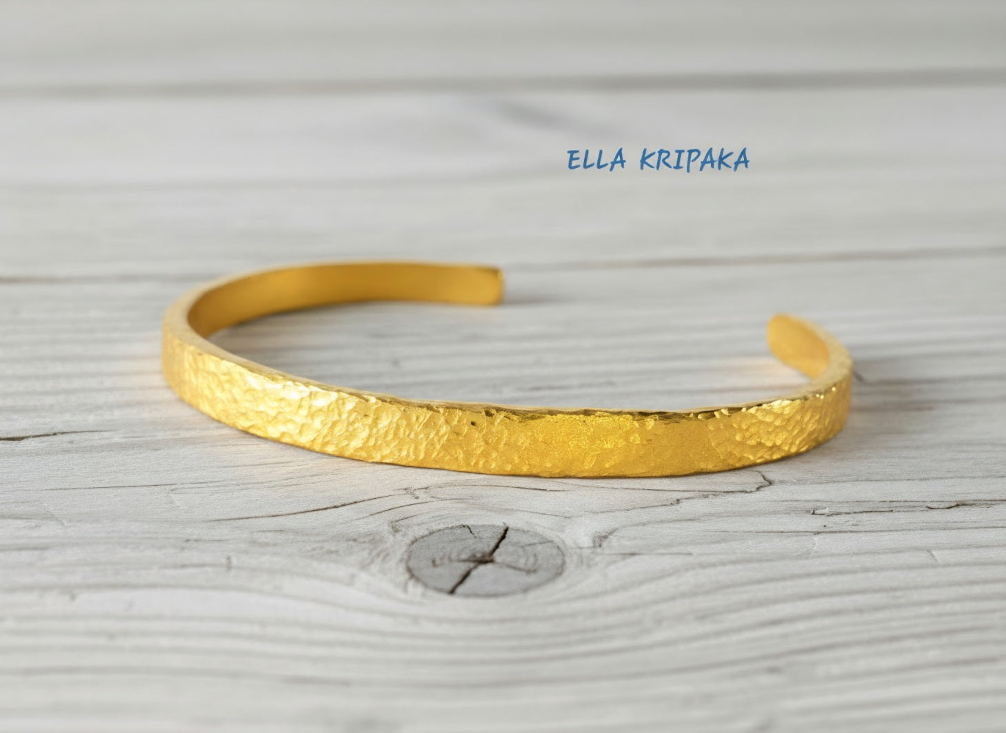 Hammered 24k 9999 gold cuff thick bracelet Ancient Rome style on an old white wooden background, artist-jeweler name 'Ella Kripaka' branding