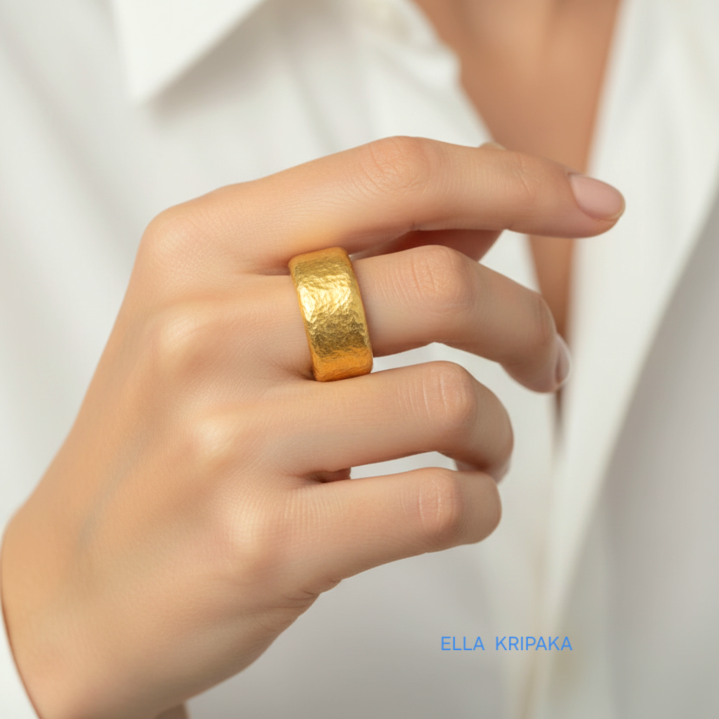 Hammered 24k Gold 9999 gold ring band thick heavy on person's finger and with textured surface on a white blurred background, branded 'Ella Kripaka'