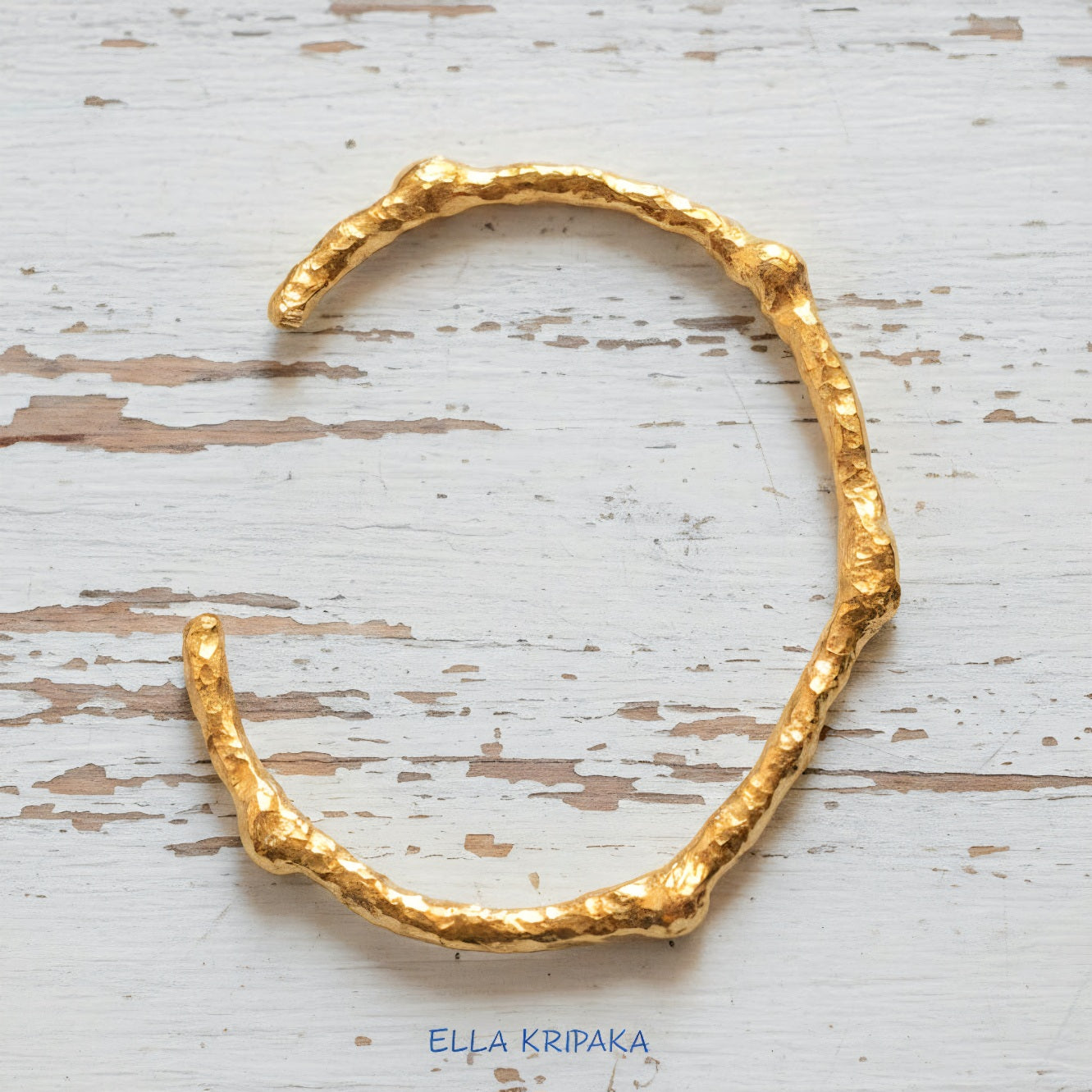 Organic hammered 24k 9999 gold bracelet uneven cuff on a old white wooden background, branding artist-jeweler name 'Ella Kripaka'