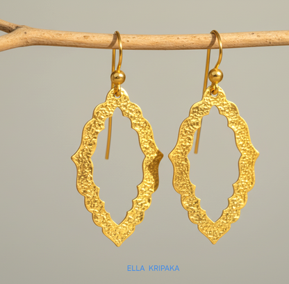 24k 9999 gold hammered Byzantine baroque convex earrings with shiny gold textures are hanging on branch on grey background, artist-jeweler's name 'Ella Kripaka'