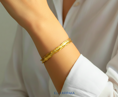 Hammered 22k gold organic textured bangle bracelet with uneven edges on model's wrist and on white blurred shirt background, and with 'Ella Kripaka' branding