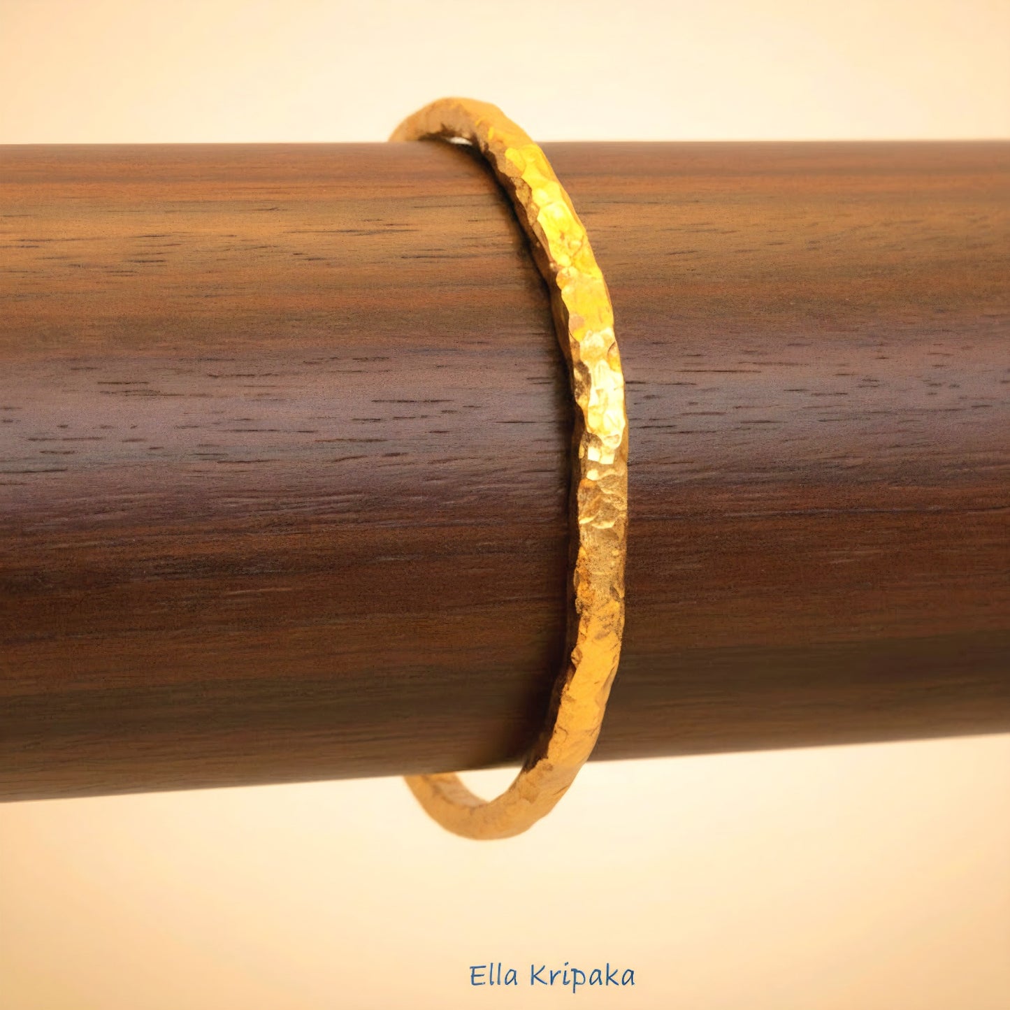 Organic 24k gold textured bangle thick bracelet with uneven edges and on a wooden stand, artist-jeweler name 'Ella Kripaka'