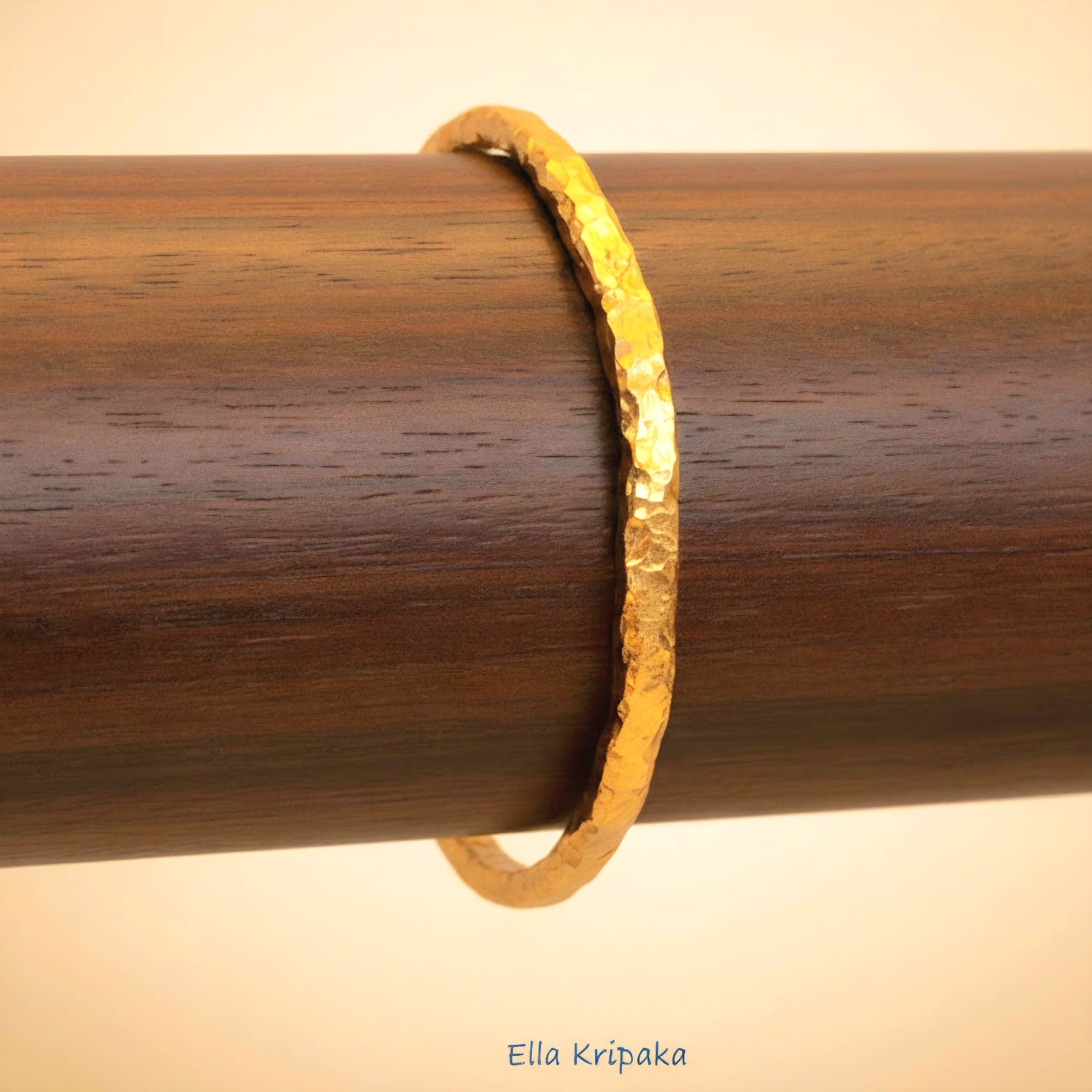 Organic 24k gold textured bangle thick bracelet with uneven edges and on a wooden stand, artist-jeweler name 'Ella Kripaka'