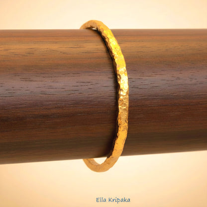 Organic 24k gold textured bangle thick bracelet with uneven edges and on a wooden stand, artist-jeweler name 'Ella Kripaka'