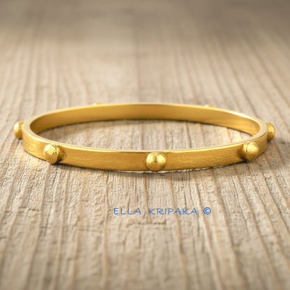 24k gold hammered bangle textured bracelet with convex rounds on light rustic wooden surface, artist 'Ella Kripaka' branding