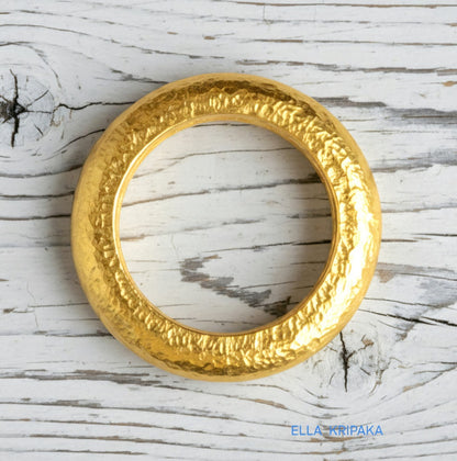 Hammered 24k 9999 Gold thick ring Ancient Rome style and with forged textured gold on a white old wooden surface, artist-jeweler's name 'Ella Kripaka' branding