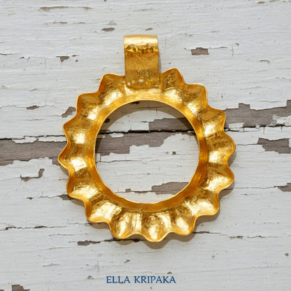 24k 9999 gold hammered convex Sun pendant on a white old wooden surface, branded 'Ella Kripaka'