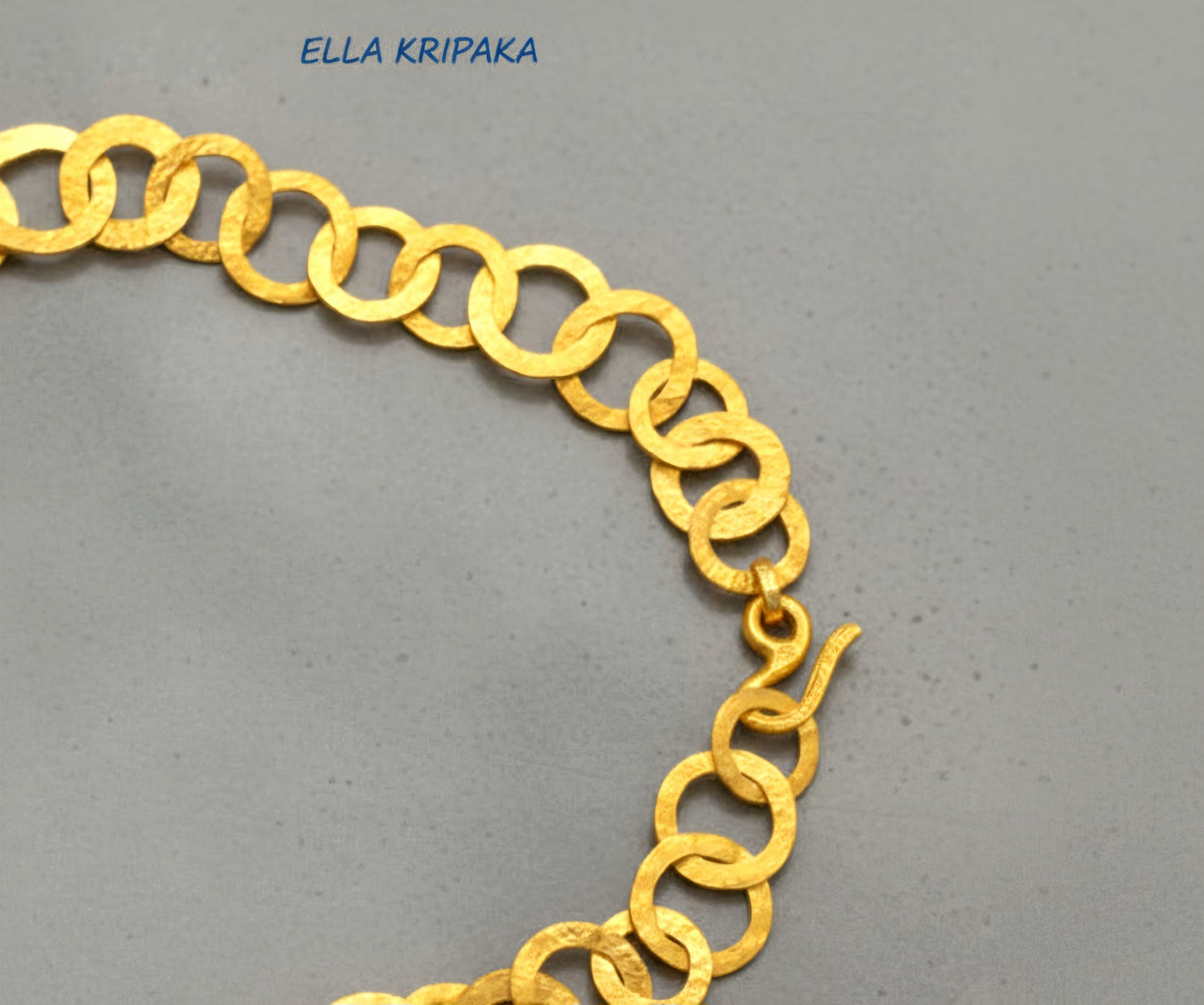 22k gold hammered chain necklace with different links and with thick hook clasp on a grey concrete surface, and with 'Ella Kripaka' branding