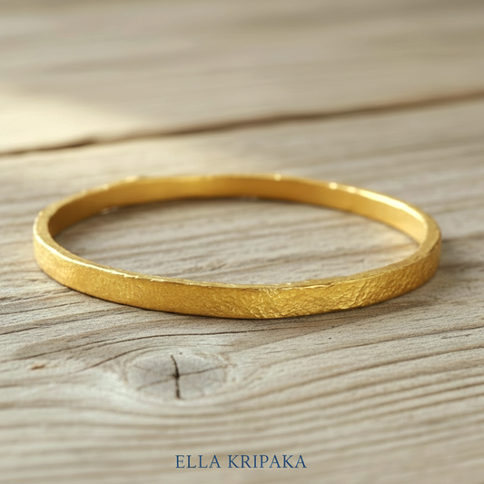 Hammered 24k 9999 gold bangle thick bracelet Ancient Rome style on a wooden background, branding artist-jeweler name 'Ella Kripaka'