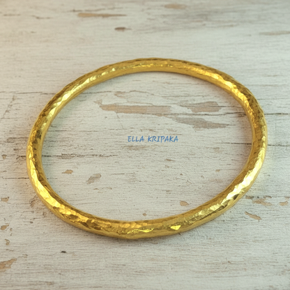 Hammered 24k 9999 gold bangle thick bracelet Ancient Rome style on a wooden background, branding artist-jeweler name 'Ella Kripaka'