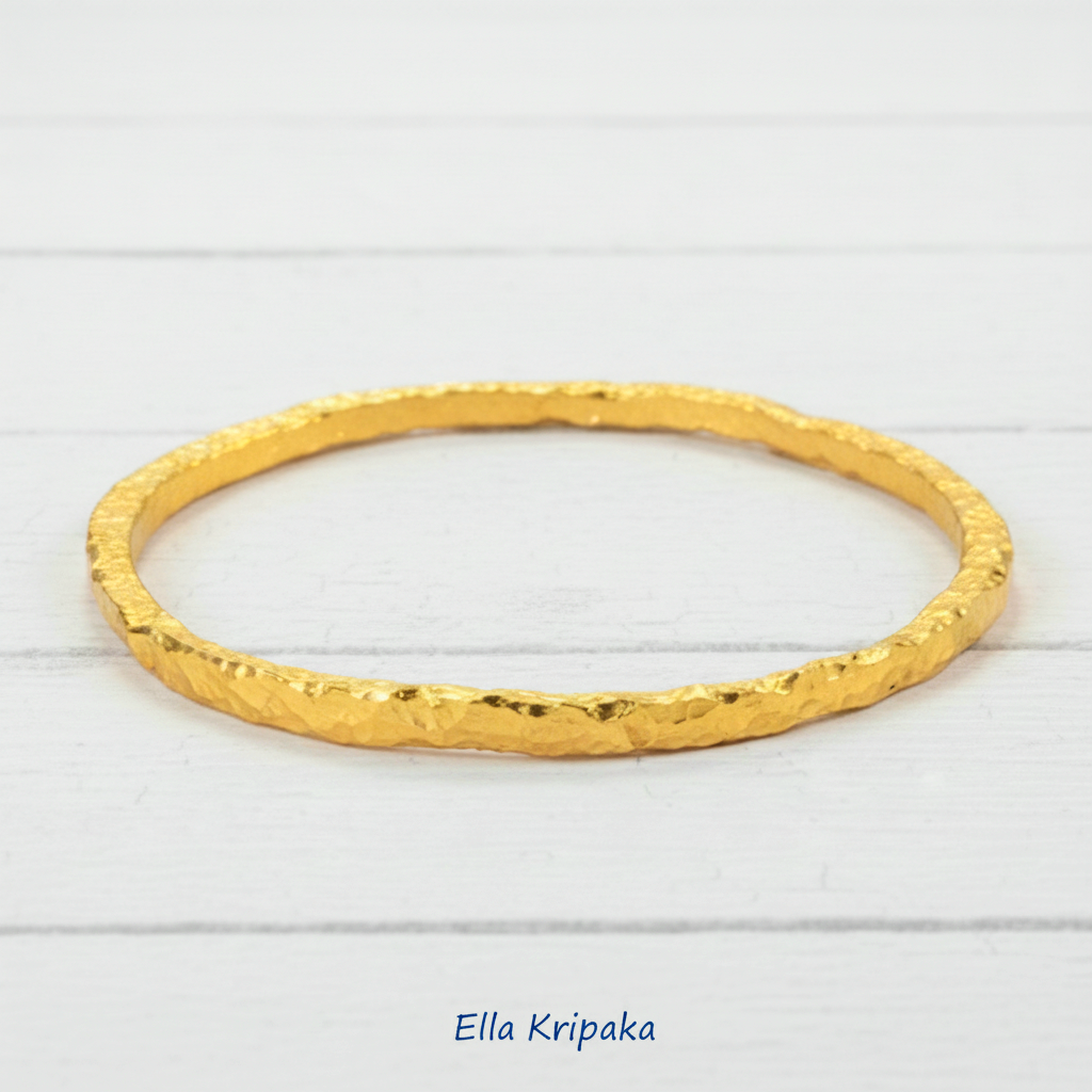 Organic 24k gold uneven bangle textured bracelet with uneven edges and on a white wooden background, artist-jeweler name 'Ella Kripaka'