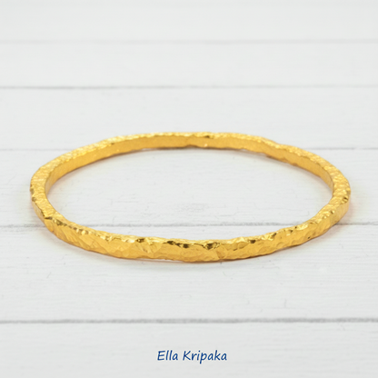 Organic 24k gold uneven bangle textured bracelet with uneven edges and on a white wooden background, artist-jeweler name 'Ella Kripaka'