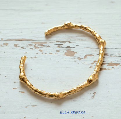 Organic hammered 24k 9999 gold bracelet uneven cuff on a old white wooden background, branding artist-jeweler name 'Ella Kripaka'