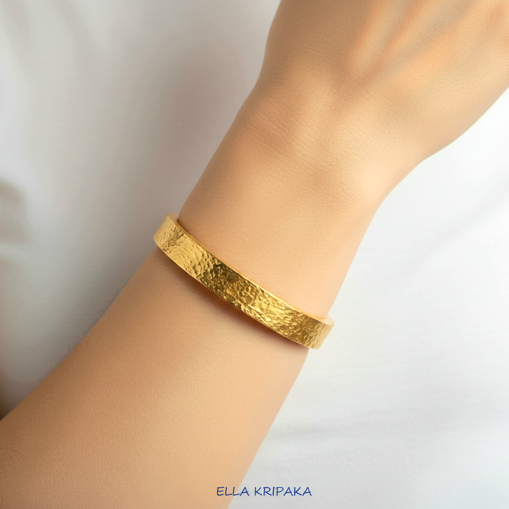 Hammered 24k Gold textured thick bangle bracelet worn by model on wrist and on white t-shirt background, artist's name 'Ella Kripaka' branding